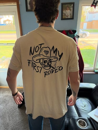 Reviewer from behind wearing the beige Rodeo Tee, showing the fit and the 'Not My First Rodeo' graphic.
