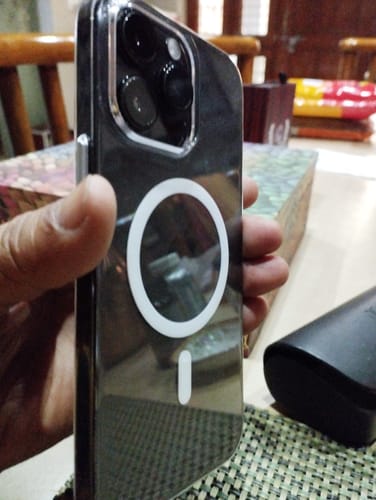 Reviewer holding a smartphone in a clear case with a white MagSafe charging symbol on the back.