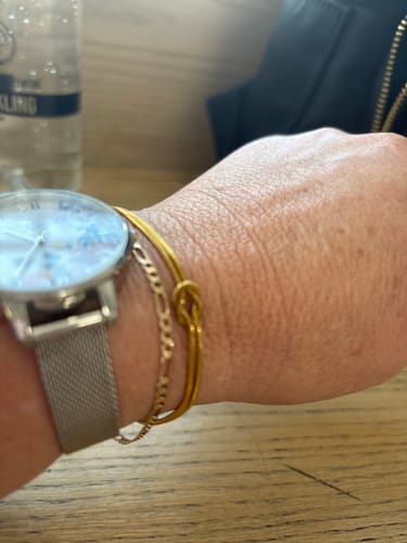 Close-up of a reviewer's wrist wearing a delicate gold-colored knot bracelet and a chain bracelet next to a silver watch.