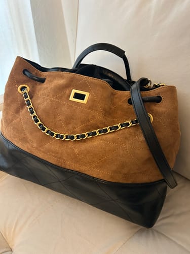 Reviewer's brown and black Contrast Handle Shoulder Bag on a couch, showing its quilted texture and gold chain detail.