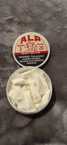 Reviewer's open tin of Sweet Nectar Nicotine Pouches filled with white pouches, with the lid beside it on a gray surface.