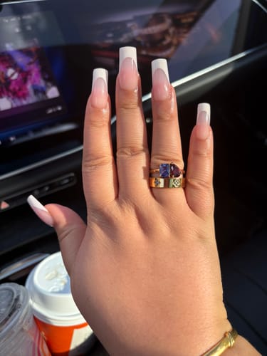 Customer's hand wearing the gold Toi Et Moi Birthstone Ring with a purple emerald-cut and a red pear-cut stone.