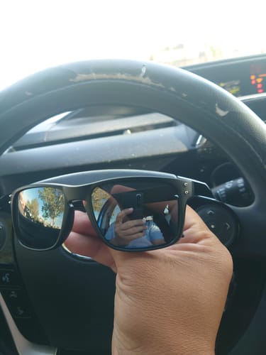 Customer holding the black 80Eighty Polarized Sunglasses with reflective lenses in their car.