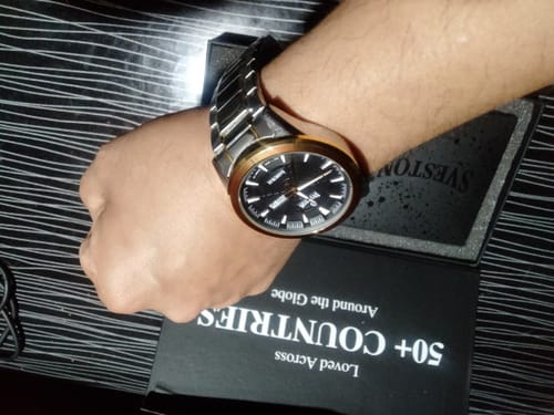 Customer wearing their two-tone Sveston Samurai watch with a bold black dial, holding it over the open product box.