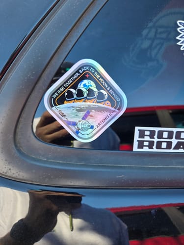 Reviewer's holographic Artemis II sticker on a car window, showing its shiny and colorful effect in the light.