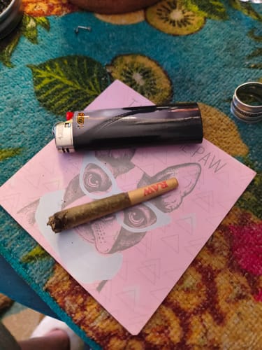 Customer's Purple Milk Pre-Roll and a black lighter resting on a pink, decorative coaster.