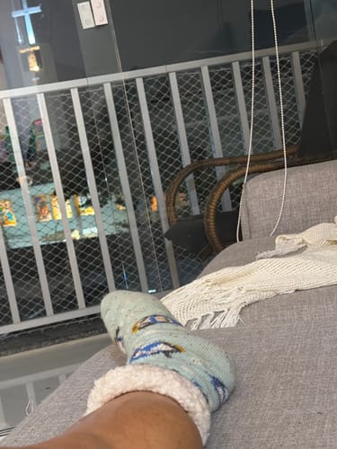 Cliente mostrando a Meia Pinguim azul claro com forro de sherpa fofo em seu pé enquanto relaxa em um sofá.