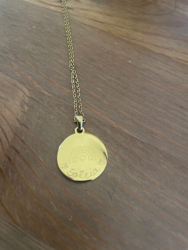 Ein Kunde zeigt seine goldene Halskette mit Gravurdesign „Rainbow“. Der runde Anhänger hat eine filigrane persönliche Gravur.