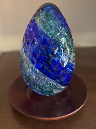 Reviewer's Dragon Egg with infused cremains, showing the blue and green scaled glass on a small stand.
