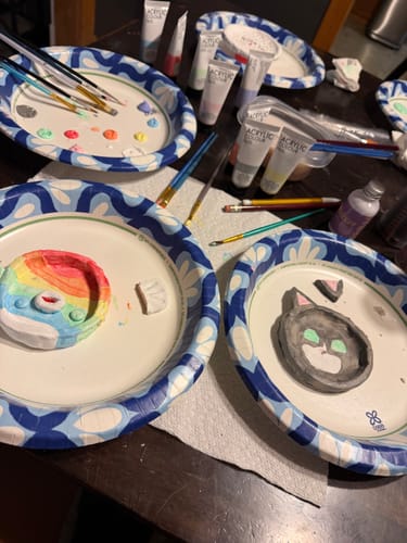 Customer's two finished and painted clay pots from the Craft Subscription Box, surrounded by paints and brushes.