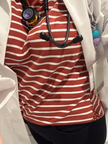 Close-up of a reviewer wearing the Striped Accented Dot Tee under a white coat, showing the dot pattern on the side.