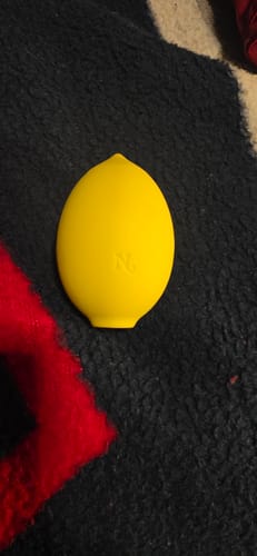 Reviewer's yellow, lemon-shaped Lem Clitoral Massager resting on a dark fleecy surface.