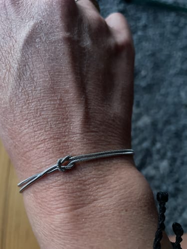 Close-up of a reviewer wearing a delicate, silver-colored knot bracelet on their wrist.
