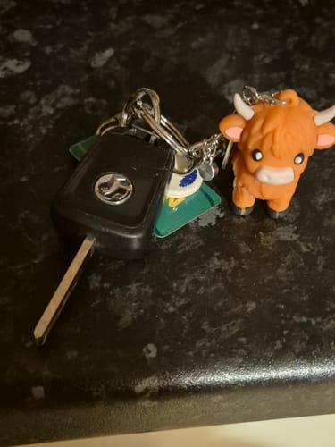 Customer's cute Highland Cow Keychain attached to a set of keys on a dark countertop.