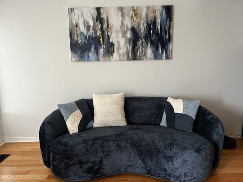 Customer's Abstract Blue & Gold canvas wall art hanging on a light wall above a dark, curved sofa.