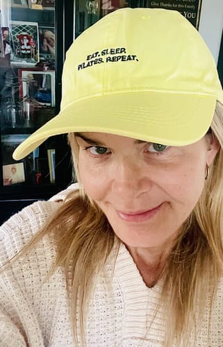 Reviewer wearing the yellow 'Eat. Sleep. Pilates. Repeat.' cap and smiling.