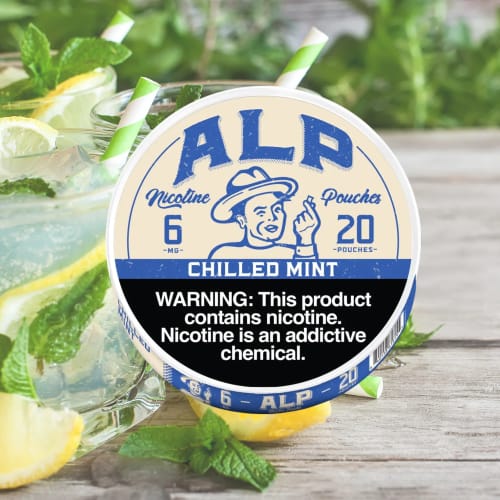 Reviewer's can of ALP Chilled Mint pouches on a wooden surface with mint and lemon drinks in the background.