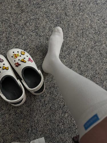 Customer's leg in a white compression sock, showing the blue brand tag at the top.