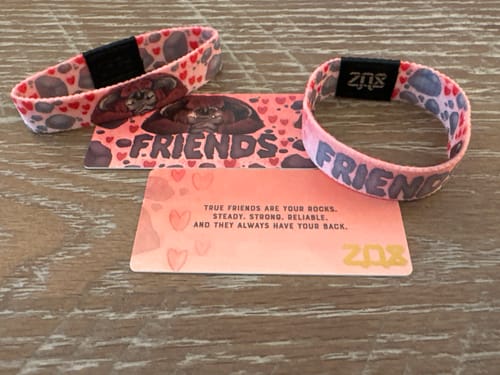 Customer's two pink Friends Labyrinth Bracelets and collector cards shown on a wooden surface.