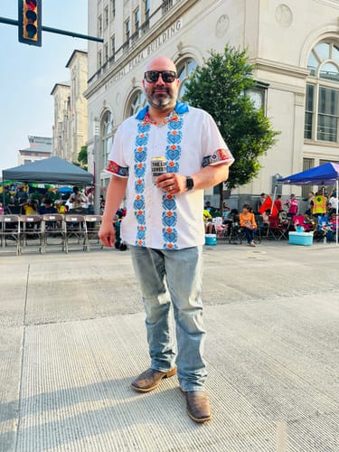 A reviewer wearing the Talavera Corazones Guayebera Shirt with jeans at an outdoor festival.