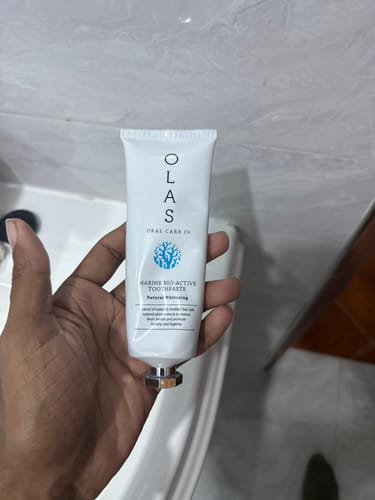 Customer holding a tube of OLAS Marine Bio-Active Whitening Toothpaste in a bathroom.