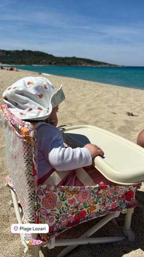 Customer's baby at the beach wearing the Paloma baby cotton hat while sitting in a patterned high chair.