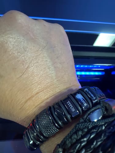 Reviewer's wrist wearing the personalized black bracelet with engraved name charms, stacked with another bracelet.