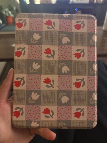A reviewer holds the Baby Tulip Kindle Case, showing off its checkered pattern with red and white tulip illustrations.