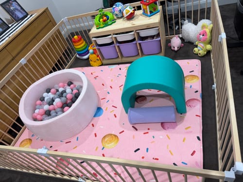 Customer's pink Mellow Mat with a donut pattern inside a playpen with a ball pit and toys.