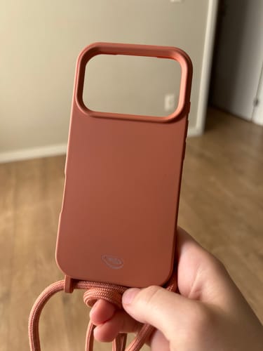 Cliente segurando a capinha para celular Cordinha Odara na cor pêssego, presa a uma alça.