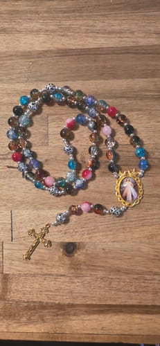 Reviewer's multicolor glass bead rosary with a brass crucifix and Divine Mercy medal laid on a wood table.
