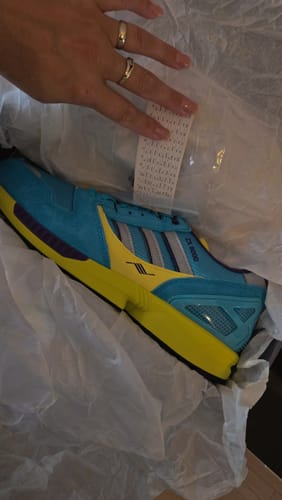 Recensent toont een nieuwe blauwe en gele sneaker in de verpakking.