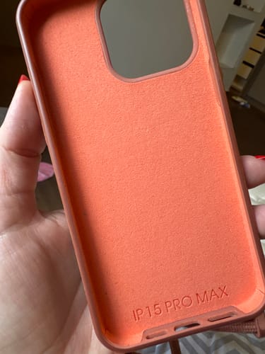 Cliente mostrando o interior aveludado da case Odara na cor Pêssego, com a inscrição para iPhone 15 Pro Max.