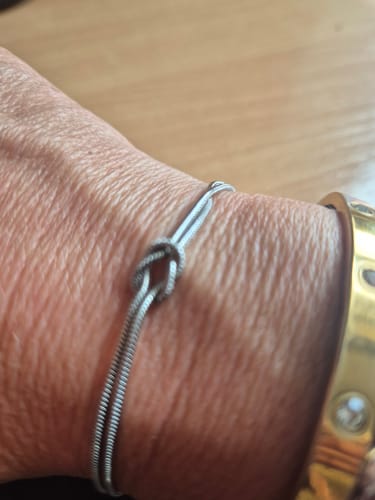 Close-up of a customer wearing the silver Forever Knot Bracelet on their wrist, next to a gold bracelet.