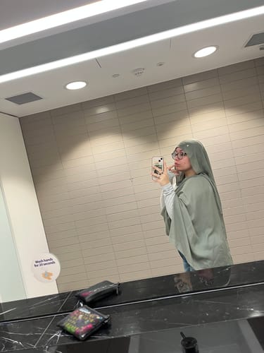 Reviewer taking a mirror selfie in a restroom, wearing the light Zeolite Premium Modal hijab draped over their shoulders.