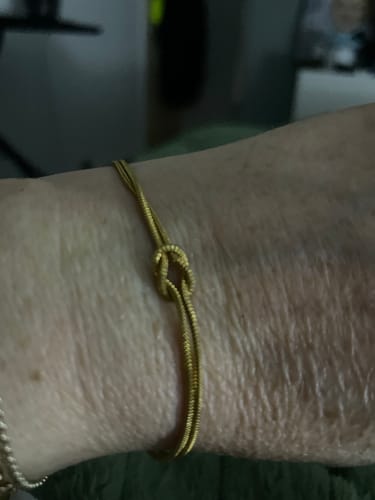 Close-up of a reviewer's wrist wearing a thin, gold-colored bracelet with a knot design.