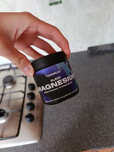 Reviewer holding a black jar of Sleep Magnesium supplement in a kitchen.