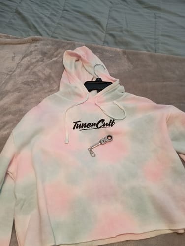 Customer's tie-dye Ladies Crop Hoodie in Cotton Candy laid flat on a bed with a small keychain on top.
