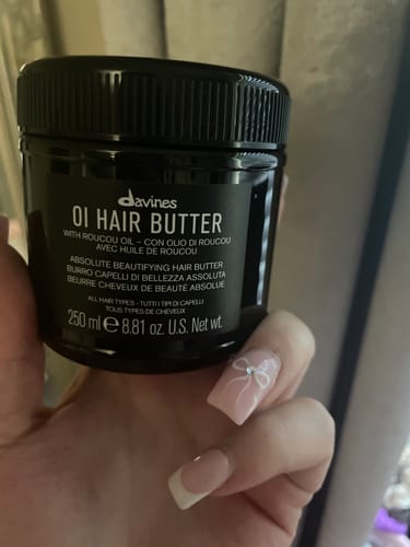 Reviewer holding the black jar of OI Hair Butter in their hand.