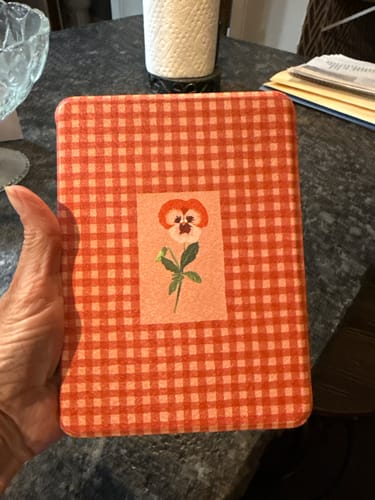 Customer holding the Autumn Pansy Kindle Case, which has a red checkered pattern and a central flower illustration.