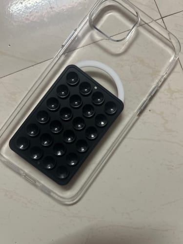 Reviewer's black StickyPod with suction cups placed next to a clear phone case on a tiled floor.