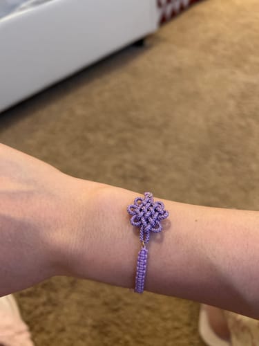 A reviewer's wrist wearing the purple BTS Arirang bracelet, showing its decorative braided knot.