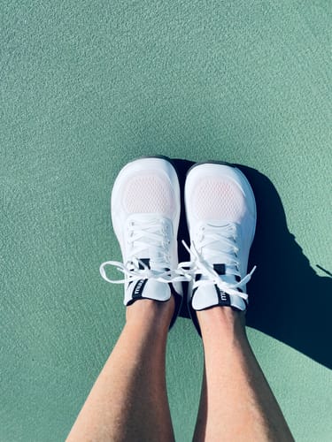 Customer's overhead view of their white CUURT Muuv court shoes on a green tennis court.