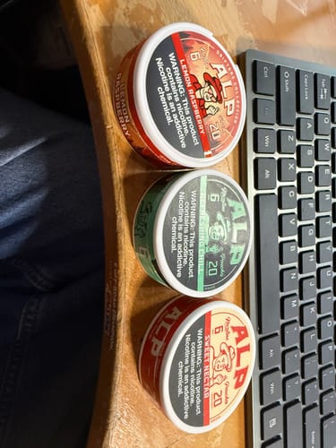 Customer's three cans of ALP nicotine pouches in Sweet Nectar, Refreshing Chill, and Lemon Raspberry flavors on a desk.
