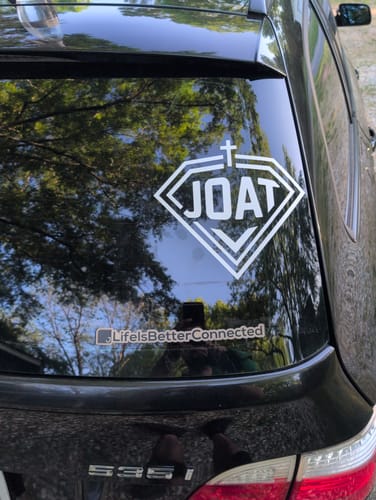 Customer's white custom printed die cut decal of their 'JOAT' logo applied to the rear window of a black car.