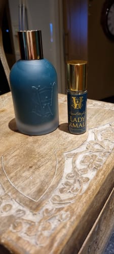 Customer's Lady Marmalade perfume shown in a large teal bottle and a smaller rollerball on a wooden table.