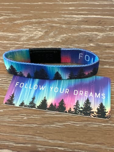 Customer's Follow Your Dreams Bracelet and matching card, both with a colorful aurora design over silhouetted trees.