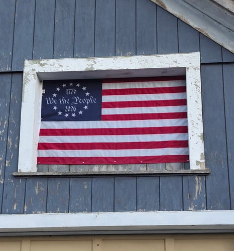 Customer's 'We The People' Betsy Ross flag displayed inside a window frame on a blue-sided building.