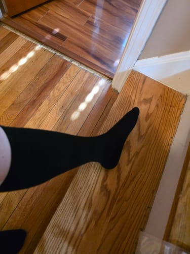 Reviewer showing the smooth fit of a black Eucalyptus Lyocell Compression Sock on their leg and foot while standing on stairs.