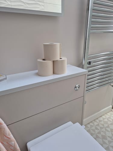 Customer's three beige rolls of Unbleached Bamboo Toilet Paper stacked in a bathroom.